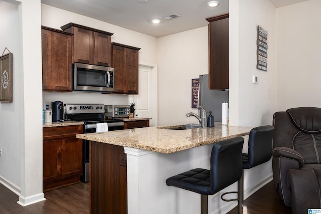 kitchen with a breakfast bar, a sink, dark wood finished floors, stainless steel appliances, and light stone countertops