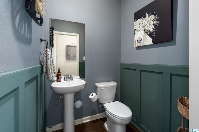 bathroom featuring a wainscoted wall, toilet, wood finished floors, a decorative wall, and a sink