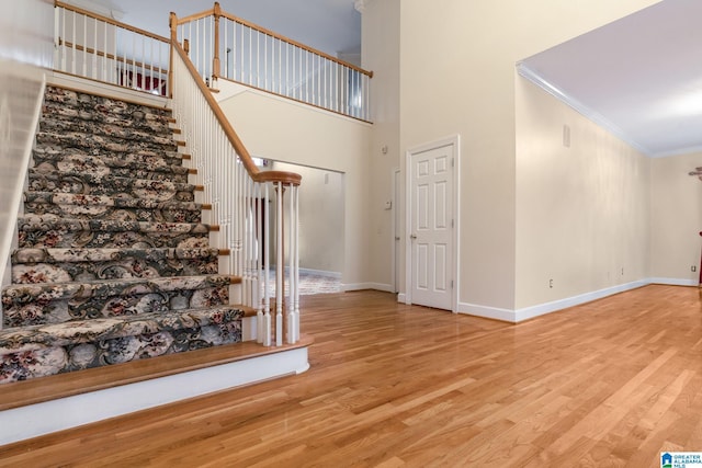 stairs with a towering ceiling, baseboards, wood finished floors, and crown molding