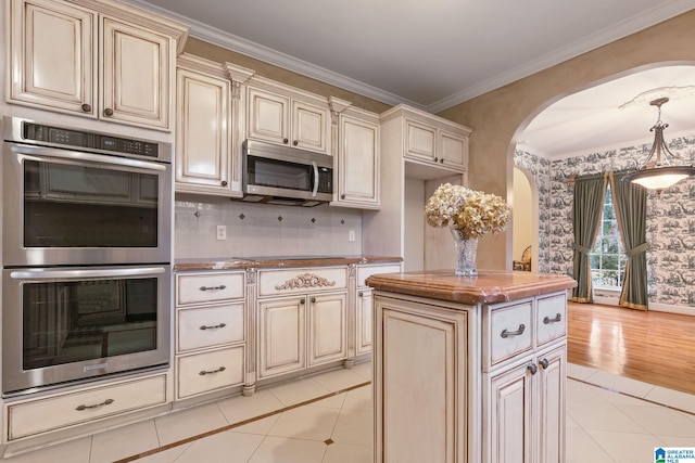 kitchen featuring crown molding, light tile patterned floors, appliances with stainless steel finishes, cream cabinets, and arched walkways