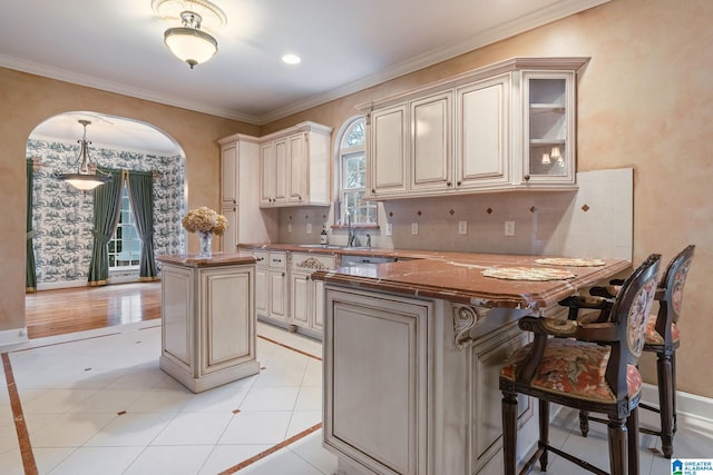 kitchen featuring backsplash, a kitchen island, light tile patterned floors, a peninsula, and cream cabinets