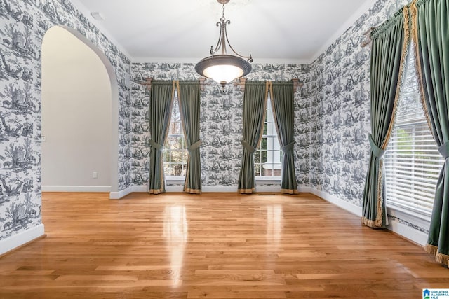 unfurnished dining area featuring wallpapered walls, wood finished floors, arched walkways, and baseboards