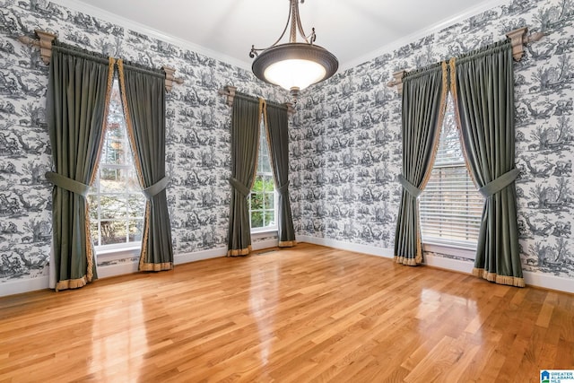 empty room featuring wood finished floors, wallpapered walls, baseboards, and ornamental molding