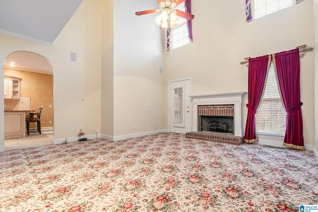 unfurnished living room with carpet, a high ceiling, a ceiling fan, and arched walkways