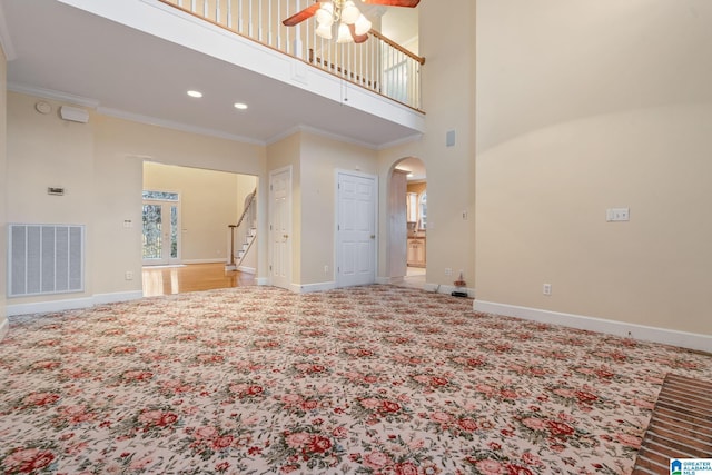 unfurnished living room featuring visible vents, crown molding, baseboards, ceiling fan, and arched walkways