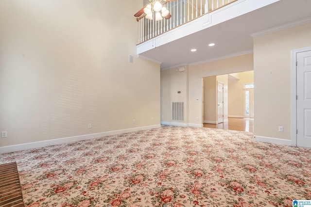 unfurnished living room with crown molding, a high ceiling, baseboards, and visible vents