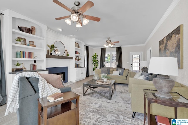 living area with light wood finished floors, a fireplace with flush hearth, built in features, ornamental molding, and a ceiling fan