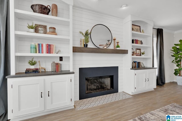 living room featuring built in features, a fireplace, light wood-type flooring, and crown molding