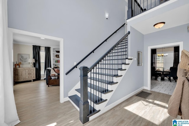 stairs with visible vents, wood finished floors, an inviting chandelier, baseboards, and a towering ceiling