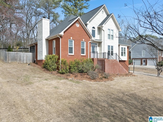 view of front of home featuring brick siding, a chimney, and fence