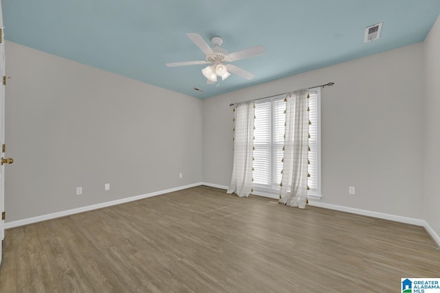 spare room featuring baseboards, wood finished floors, visible vents, and ceiling fan