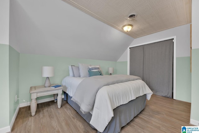 bedroom with visible vents, light wood-style flooring, lofted ceiling, and baseboards