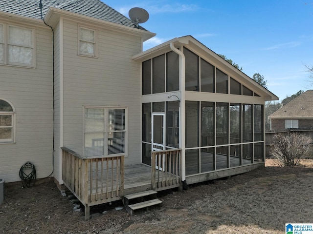 rear view of property featuring a wooden deck, a sunroom, and a shingled roof