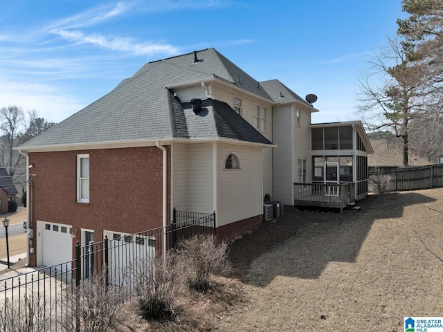 view of home's exterior featuring a shingled roof, fence, central air condition unit, a sunroom, and an attached garage