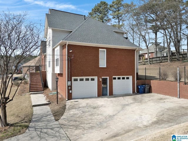 view of home's exterior with a shingled roof, stairs, concrete driveway, a garage, and brick siding