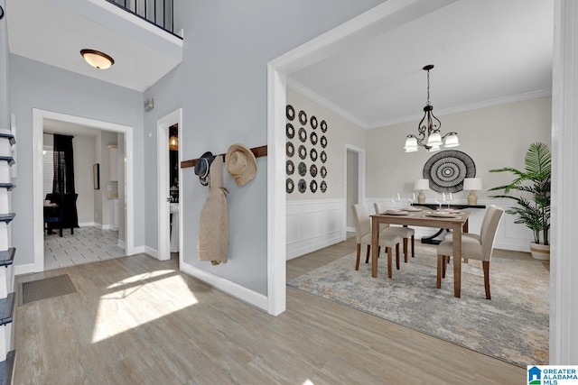 dining room with crown molding, a notable chandelier, wood finished floors, and a wainscoted wall