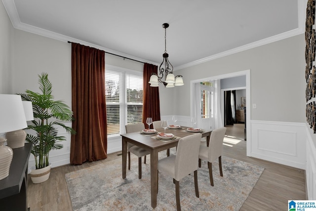 dining space with light wood-style floors, an inviting chandelier, ornamental molding, and wainscoting