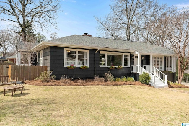 ranch-style house featuring roof with shingles, a front yard, and fence