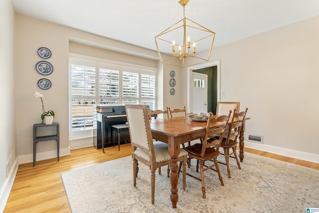 dining space with visible vents, wood finished floors, baseboards, and a chandelier