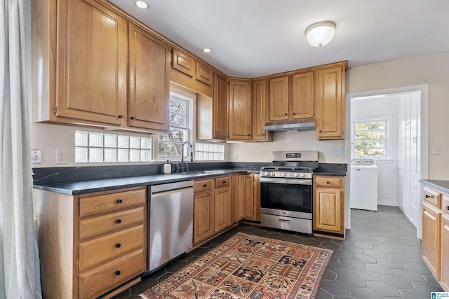 kitchen with dark countertops, under cabinet range hood, stainless steel appliances, washer / clothes dryer, and a sink