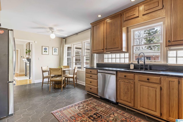 kitchen with a sink, stainless steel appliances, dark countertops, and ceiling fan