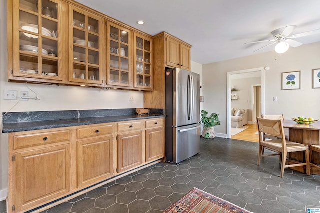 kitchen with dark tile patterned flooring, a ceiling fan, freestanding refrigerator, glass insert cabinets, and baseboards