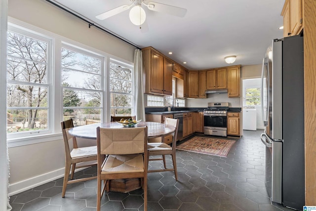 kitchen with dark countertops, ceiling fan, under cabinet range hood, stainless steel appliances, and a sink