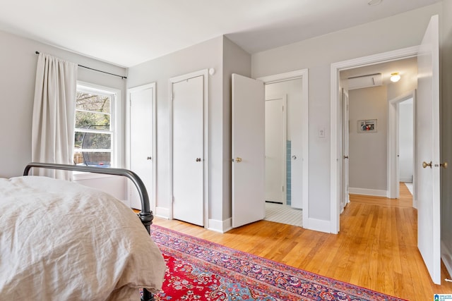 bedroom featuring baseboards, multiple closets, and light wood finished floors