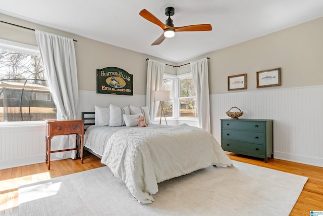 bedroom featuring ceiling fan, wood finished floors, and wainscoting