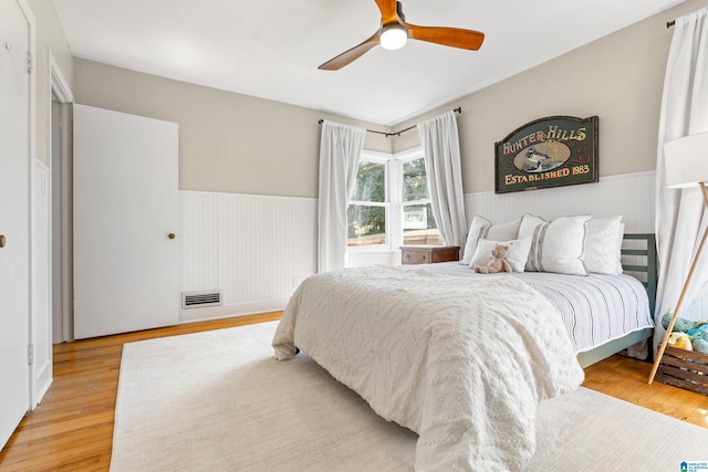 bedroom featuring visible vents, wainscoting, light wood-type flooring, and ceiling fan