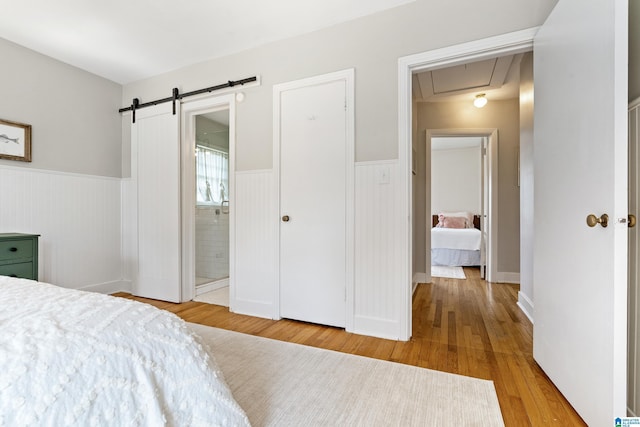 bedroom featuring wainscoting, attic access, a barn door, and wood finished floors