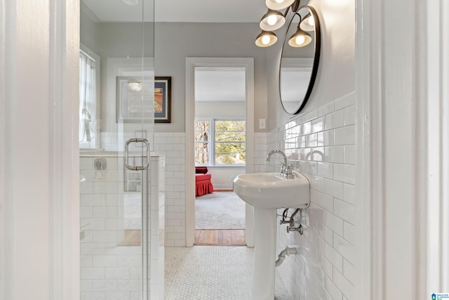 full bath featuring tile patterned floors, wainscoting, tile walls, and a shower with door