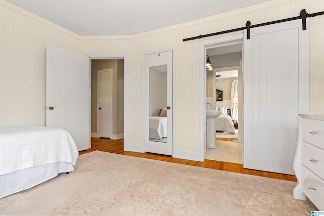 bedroom with a barn door, crown molding, and wood finished floors