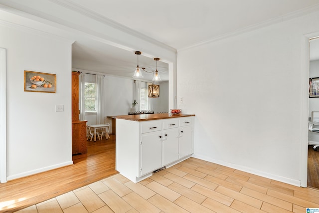 kitchen featuring baseboards, ornamental molding, a peninsula, light wood-style floors, and white cabinets