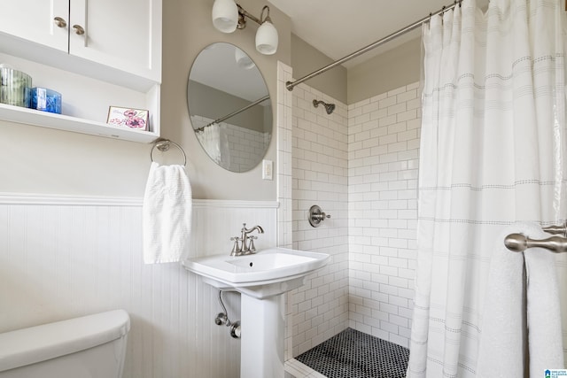 full bath featuring a tile shower, a wainscoted wall, and toilet