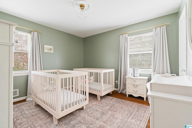 bedroom with a crib, wood finished floors, visible vents, and baseboards