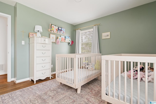 bedroom featuring visible vents, a crib, baseboards, and wood finished floors