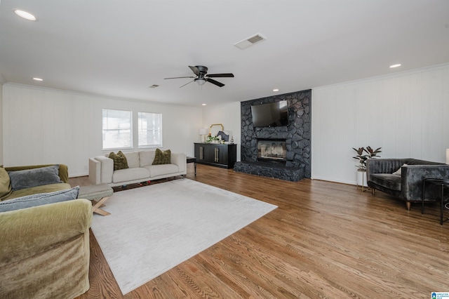 living room featuring visible vents, crown molding, a fireplace, wood finished floors, and a ceiling fan