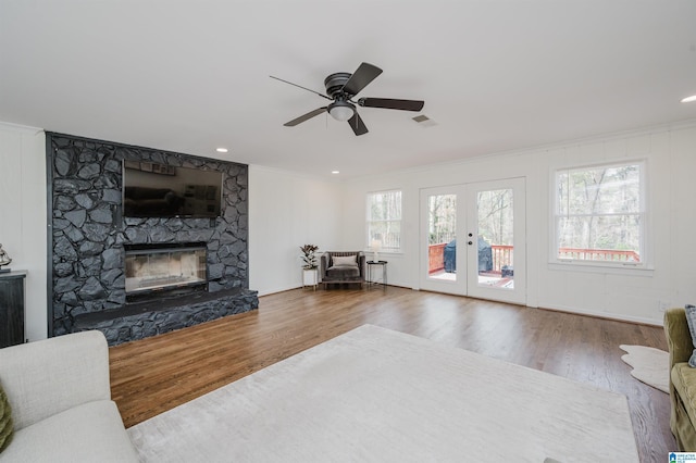 living room with a stone fireplace, crown molding, a ceiling fan, and wood finished floors