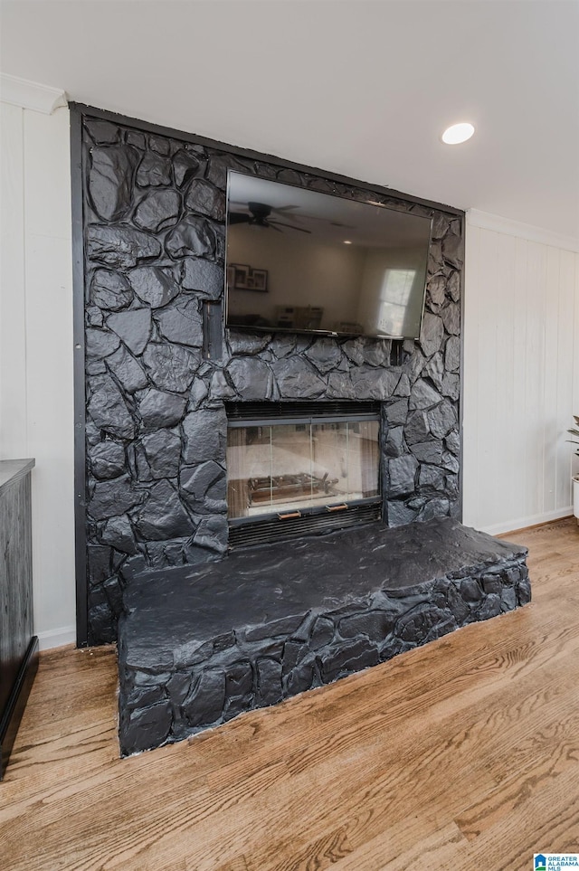 interior details with a stone fireplace, wood finished floors, and a ceiling fan