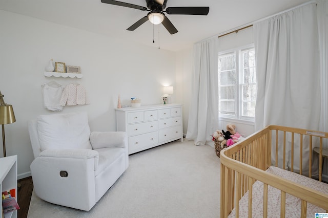 bedroom featuring a nursery area, light colored carpet, and ceiling fan