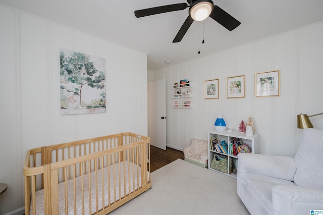 bedroom with ceiling fan, a nursery area, and wood finished floors