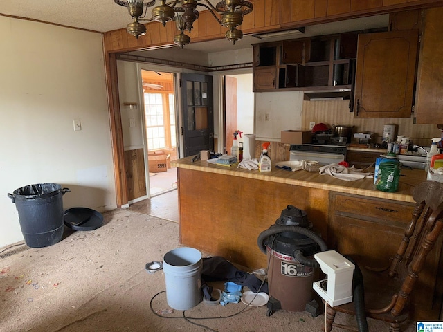 kitchen with stove, a peninsula, a chandelier, and brown cabinetry