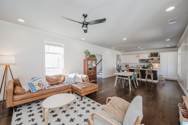 living room with stairway, a ceiling fan, visible vents, dark wood-style flooring, and ornamental molding