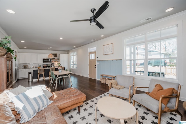 living room with dark wood-style flooring, visible vents, a ceiling fan, and ornamental molding