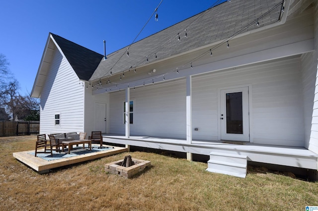 rear view of house with a shingled roof, fence, an outdoor fire pit, a lawn, and a deck