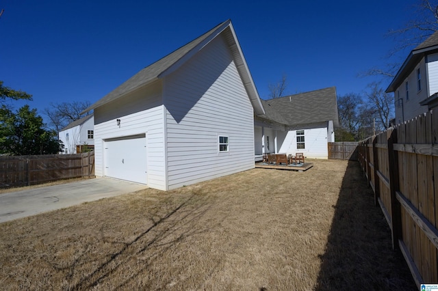 view of home's exterior with a shingled roof, concrete driveway, a lawn, a fenced backyard, and an attached garage