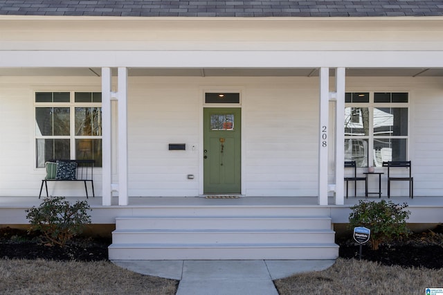 entrance to property featuring covered porch and a shingled roof