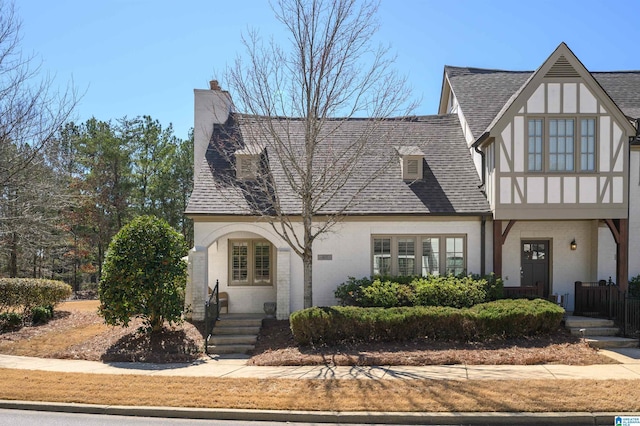 tudor house featuring stucco siding, a chimney, and a shingled roof