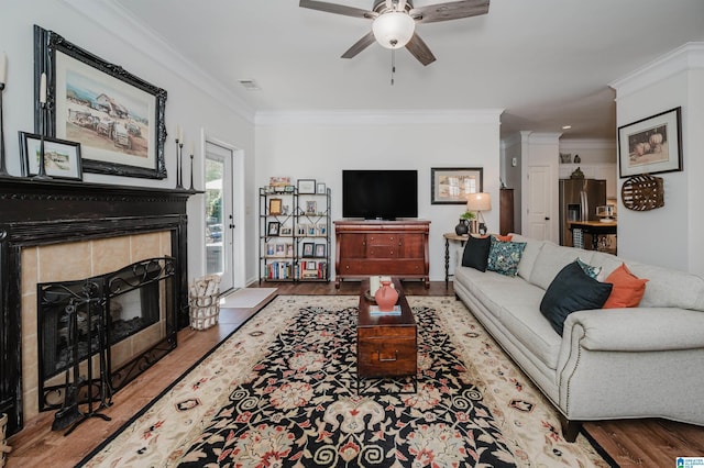 living room with visible vents, wood finished floors, crown molding, and a tile fireplace